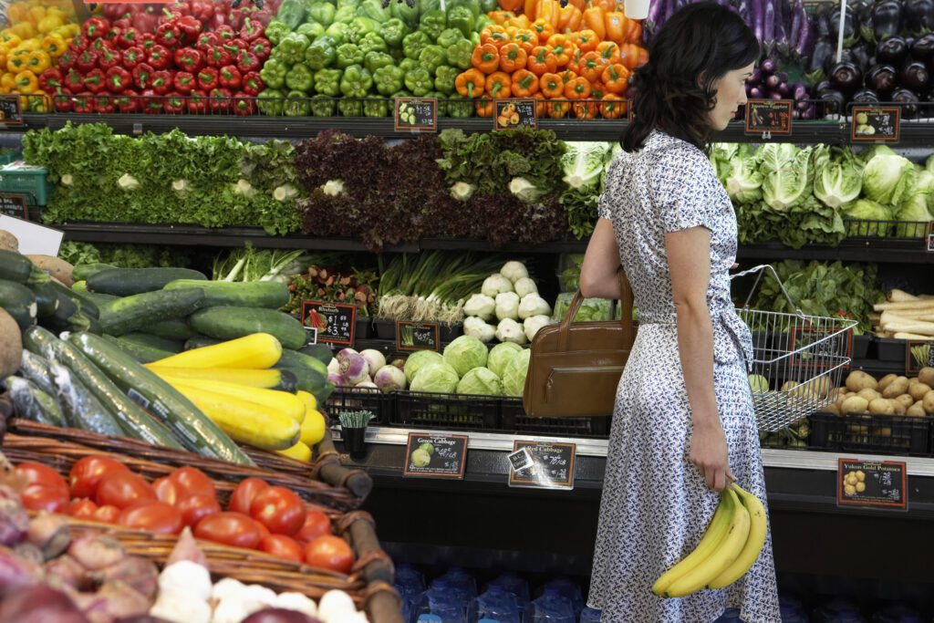 Chica sosteniendo platanos mientras compra verdura